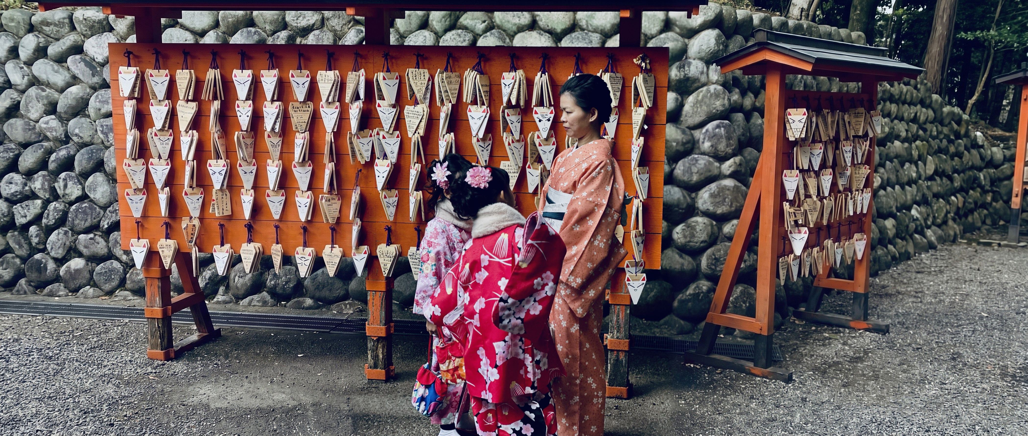 Mergaitės ir moteris su kimono prie lapių lentelių Fušimi Inari šventykloje
